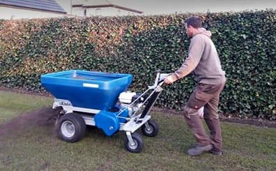 man using top dressing machine on lawn